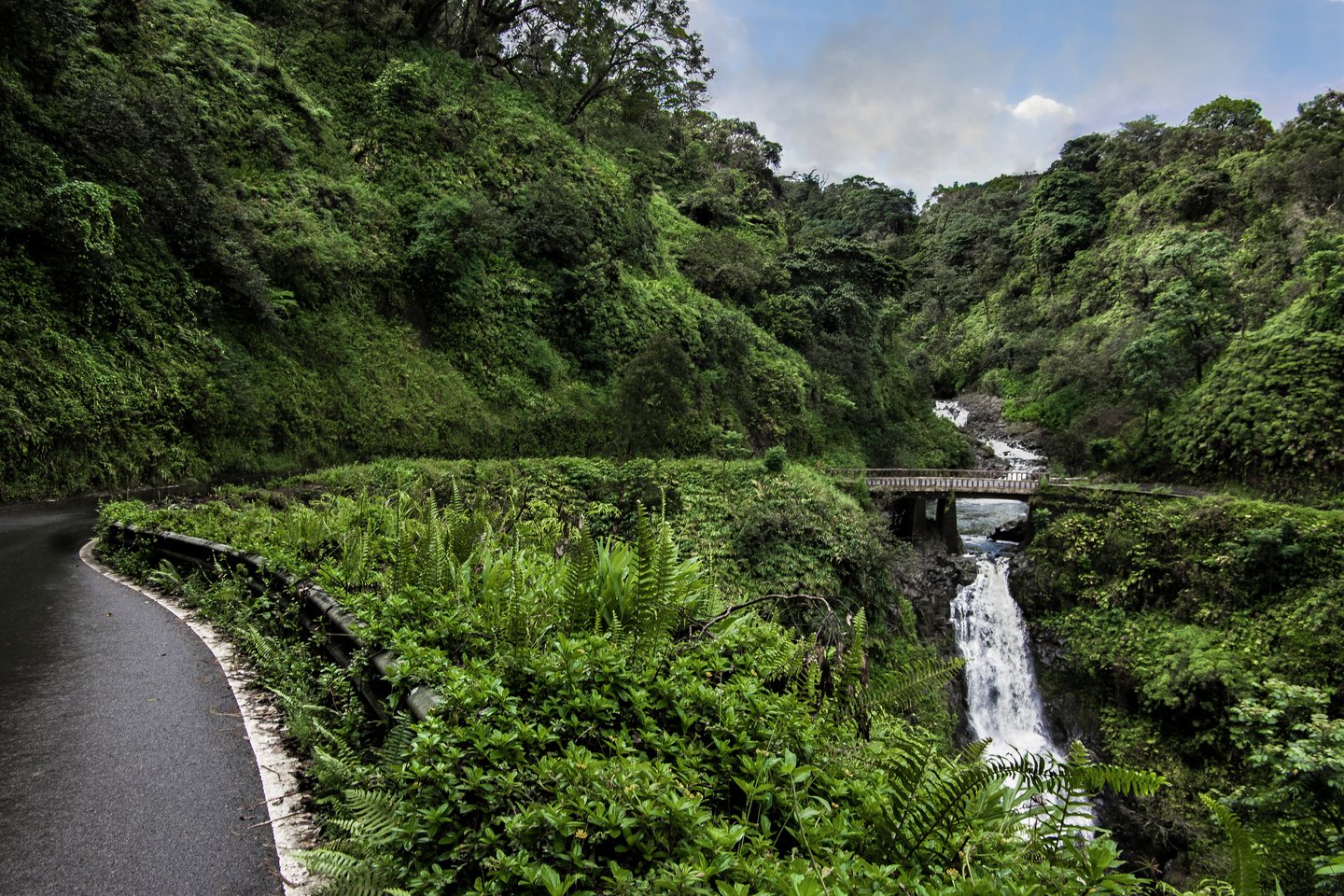 The Hana Highway turns to cross a one lane bridge beside a waterfall on the north coast of Maui