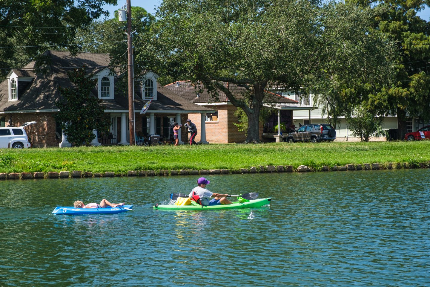 Man paddling kayak and towing child on Bayou St. John with man and woman boxing in background