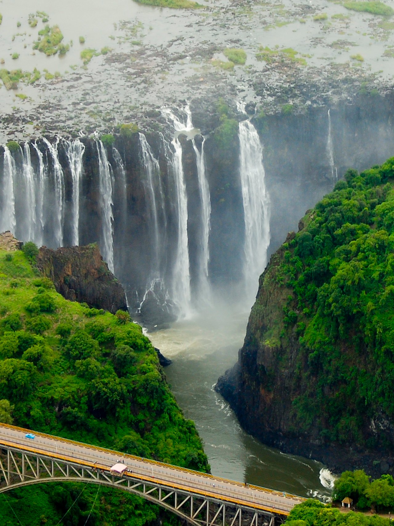 An aerial view of the immense Victoria Falls with a bridge in the foreground