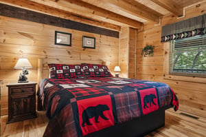 Cozy log cabin bedroom with rustic charm, featuring bearthemed bedding and warm wood surroundings for your peaceful mountain retreat.