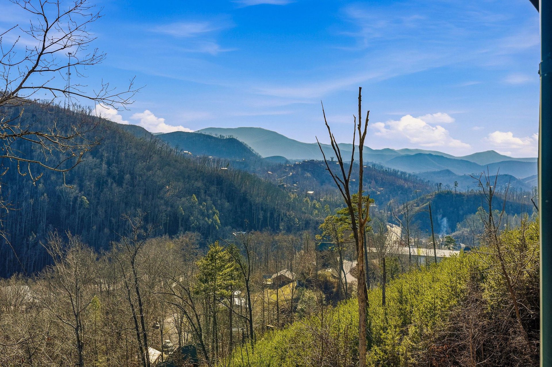 Stunning mountain vista showcases rolling forested hills and peaceful valley below under bright blue skies.