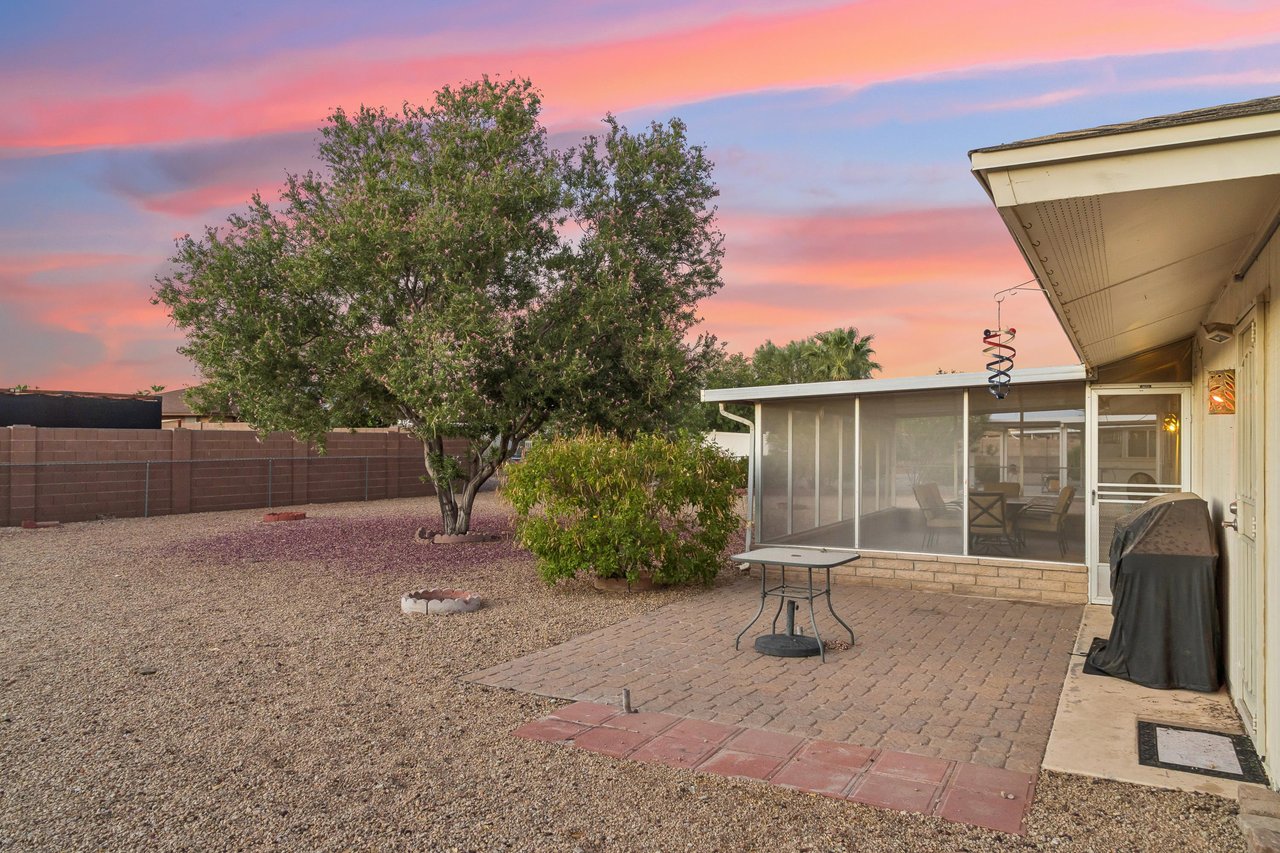 Large outdoor space in backyard with BBQ, additional table, and fencedin yard.