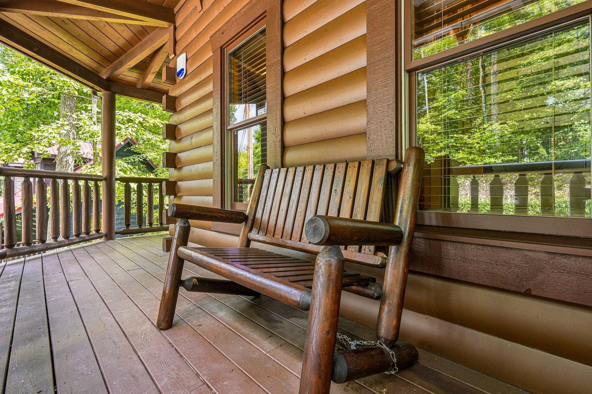 Relax on your private covered porch with a handcrafted log bench, surrounded by tall trees and gentle forest light filtering through the windows.