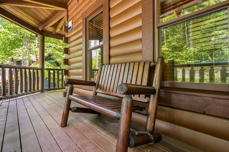 Relax on your private covered porch with a handcrafted log bench, surrounded by tall trees and gentle forest light filtering through the windows.