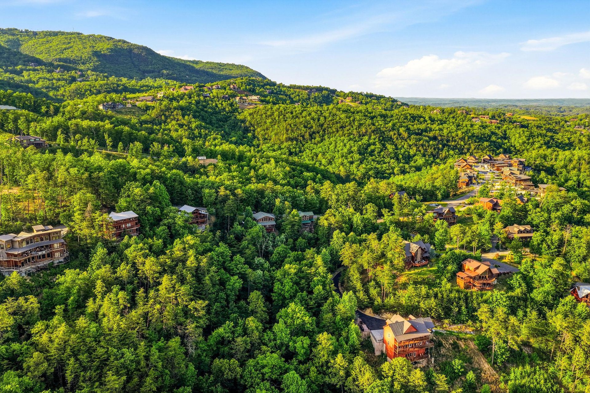 An aerial view captures cabin rentals nestled among lush mountain forests, offering a peaceful retreat surrounded by natural beauty and wooded hillsides.
