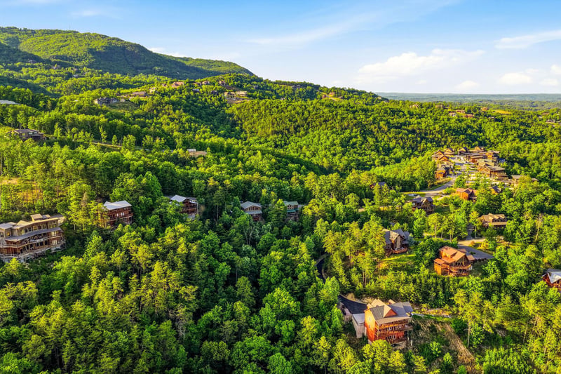An aerial view captures cabin rentals nestled among lush mountain forests, offering a peaceful retreat surrounded by natural beauty and wooded hillsides.