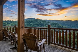 A stunning mountain sunset unfolds beyond the propertys covered deck, where forested hills frame the surrounding area in this peaceful, naturally scenic region.