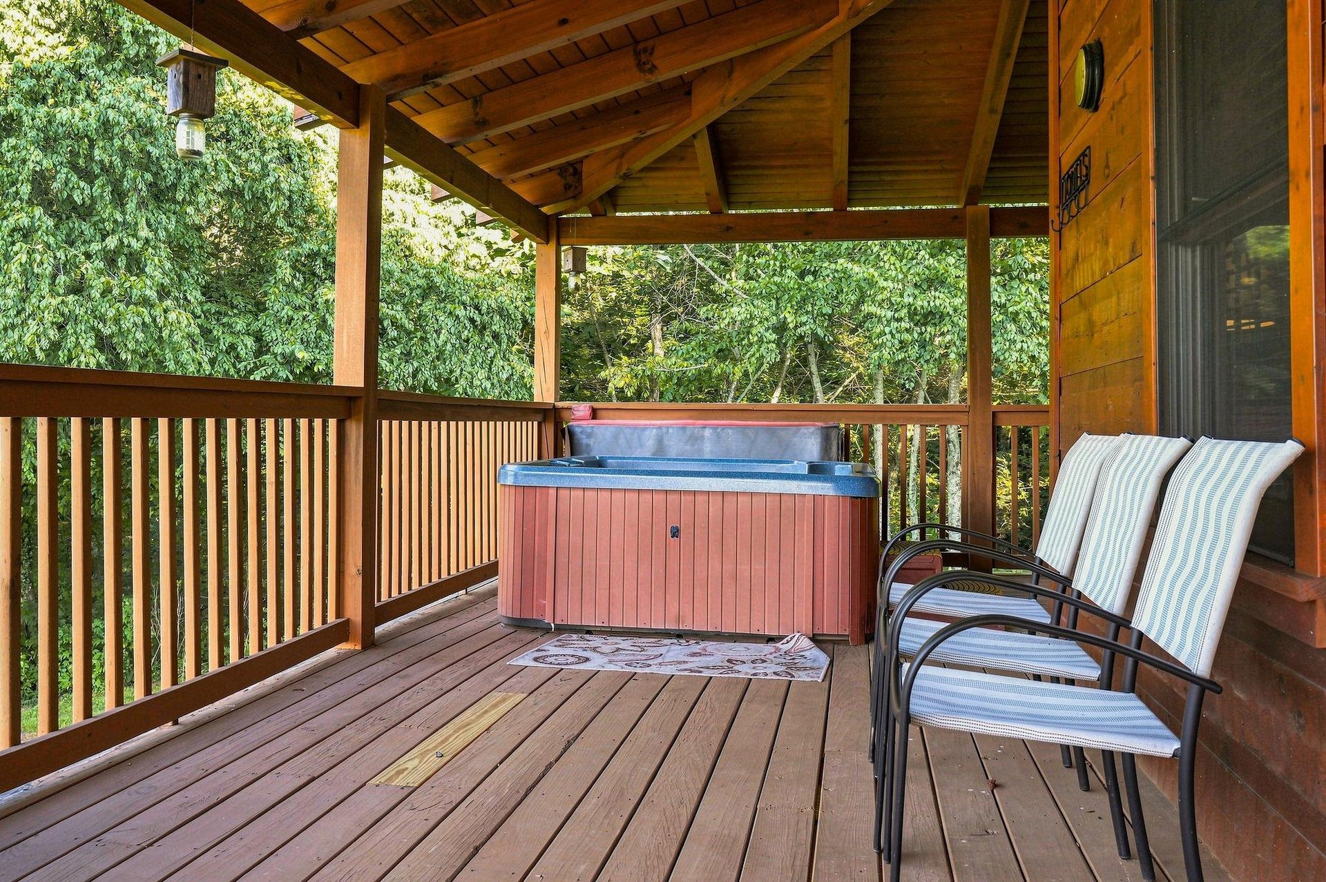 Soak beneath a vaulted woodbeam ceiling on your private covered deck. The hot tub sits ready, chairs await, and trees surround you in quiet seclusion—your perfect escape.
