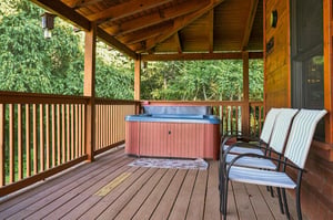 Soak beneath a vaulted woodbeam ceiling on your private covered deck. The hot tub sits ready, chairs await, and trees surround you in quiet seclusion—your perfect escape.