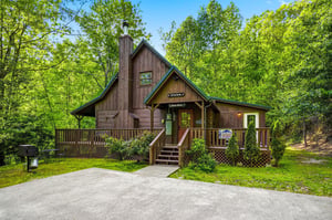 Charming wooden cabin nestled among towering trees, featuring a welcoming front porch and peaceful forest setting for your mountain getaway.