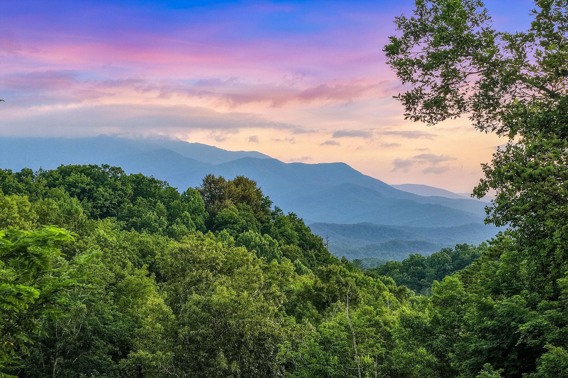 Stunning mountain vistas surrounded by lush forested hills create a peaceful natural setting as the sun sets over the landscape.
