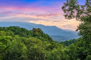 Stunning mountain vistas surrounded by lush forested hills create a peaceful natural setting as the sun sets over the landscape.
