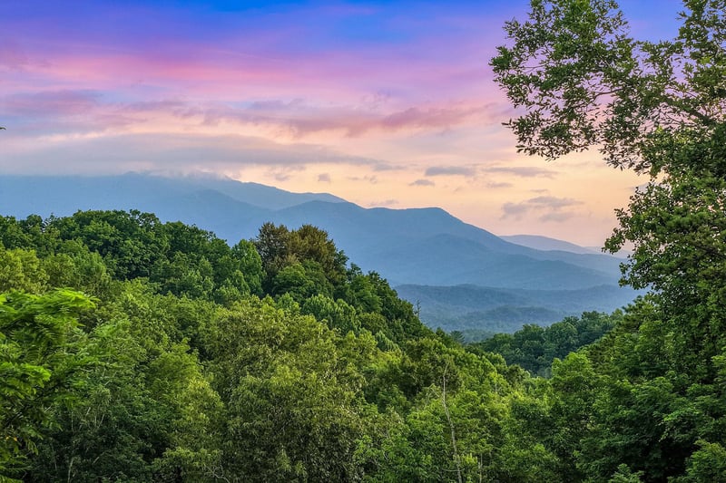 Stunning mountain vistas surrounded by lush forested hills create a peaceful natural setting as the sun sets over the landscape.