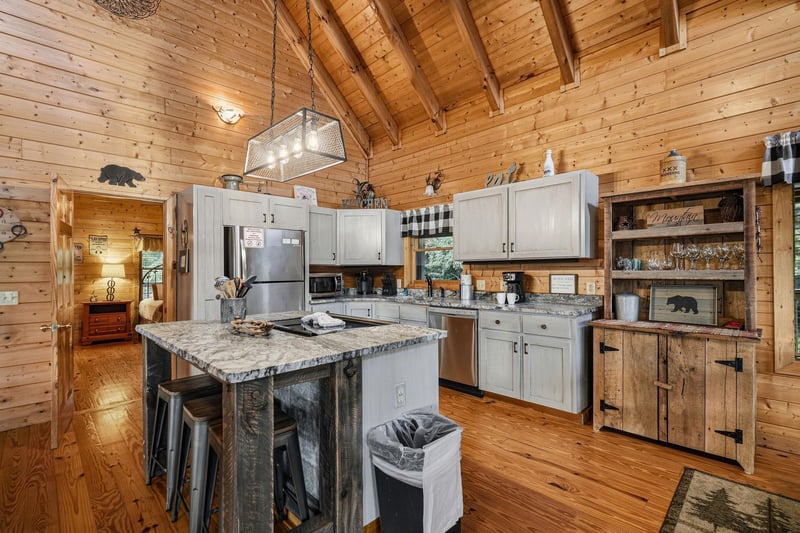 This rustic cabin kitchen invites you to cook and gather under soaring woodbeam ceilings, blending cozy charm with modern appliances and a granitetopped island perfect for morning coffee.