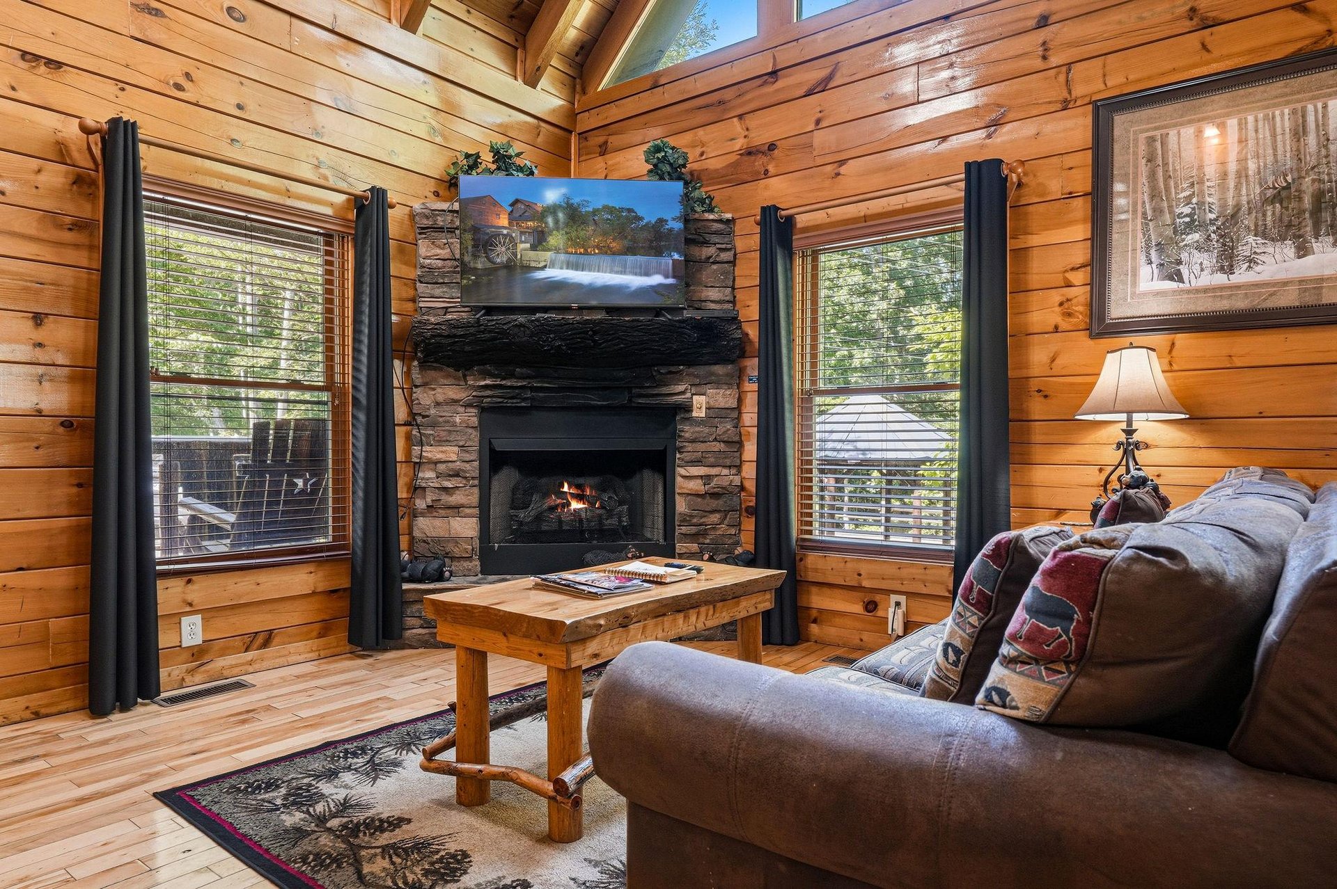 Sink into plush seating beside the glowing fireplace while natural light streams through tall windows, framing your peaceful woodland retreat with warmth and rustic charm.