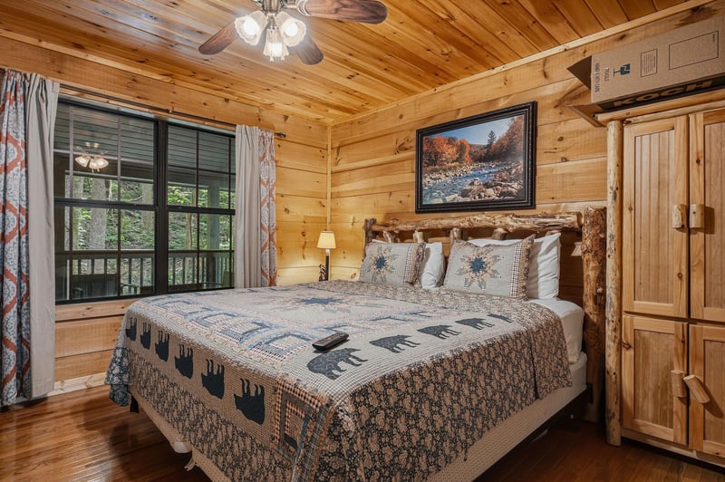 Sink into rustic comfort in your cozy bedroom, where warm wood walls and a handcrafted log bed invite restful nights. Wake to forest views through charming windows and enjoy cool comfort from the mini