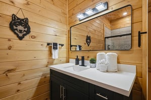 Freshen up in your cozy cabin bathroom featuring warm wood walls, modern vanity with premium amenities, and mountain lodge charm.