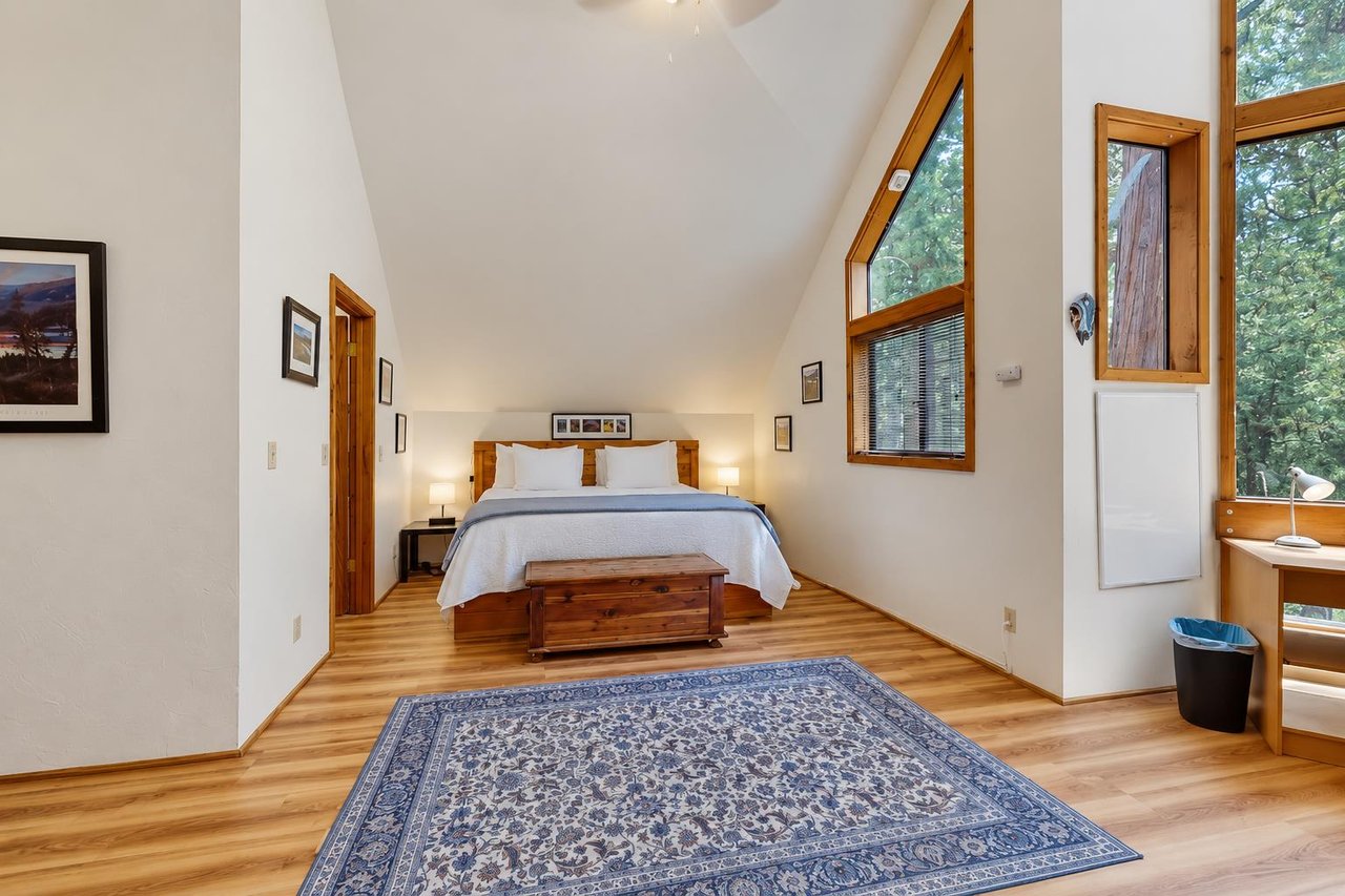 Retreat to the spacious primary bedroom, with a comfortable king bed, vaulted ceilings, and big windows framing the surrounding forest.