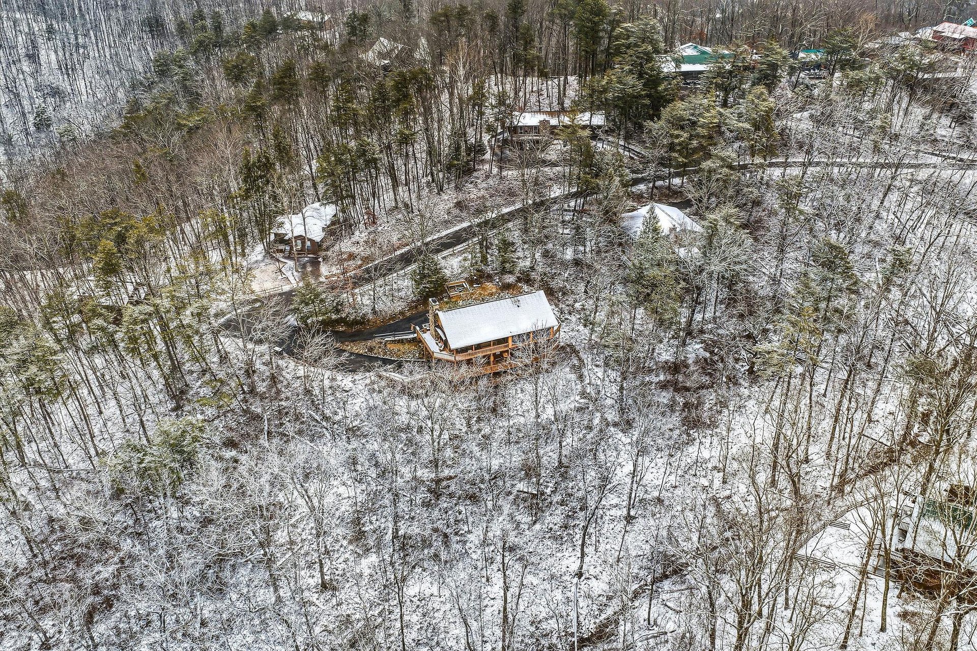 Aerial winter view of a secluded mountain cabin nestled among snowcovered trees and surrounding forest properties.