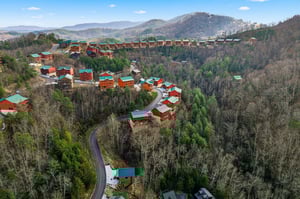 Aerial view of mountain cabins nestled among rolling hills and forested valleys in a scenic vacation rental community.