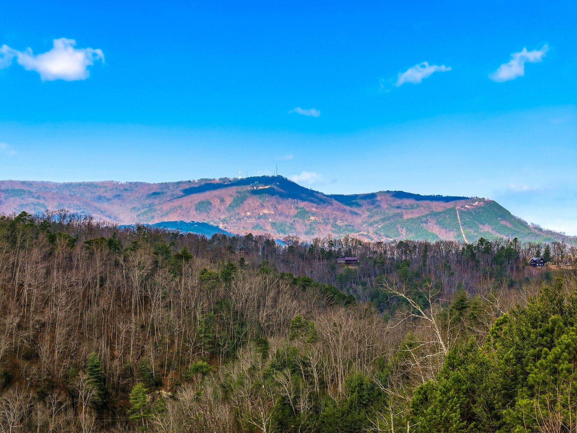 Rolling mountains display vibrant autumn colors under a brilliant blue sky with scattered white clouds in this scenic landscape view.