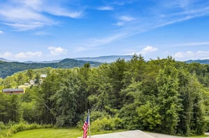Expansive mountain vistas stretch across lush green valleys, offering sweeping views of layered ridges beneath vibrant blue skies and scattered clouds.