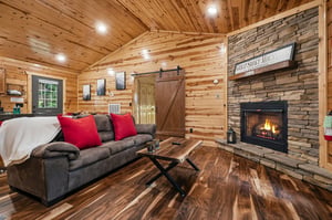 Curl up by the crackling fireplace in this cozy cabin retreat. Warm wood beams, rustic stone accents, and plush seating invite you to unwind after a day of adventure, with pops of red adding charm to 