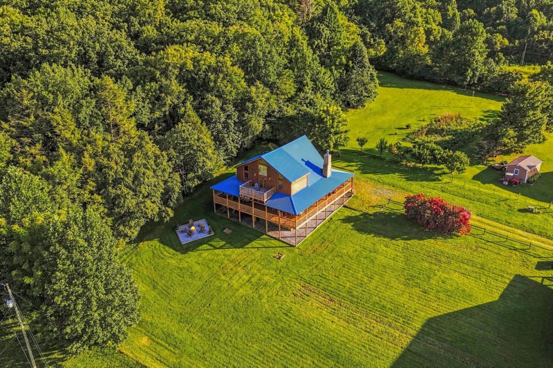 Aerial view captures the vacation rental surrounded by lush green lawn and mature trees, with an outbuilding nestled nearby for added storage or amenities.
