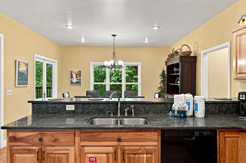 Your fully equipped kitchen features granite countertops, stainless steel sink, and warm wood cabinetry—perfect for preparing homecooked meals with natural light streaming through windows overlooking