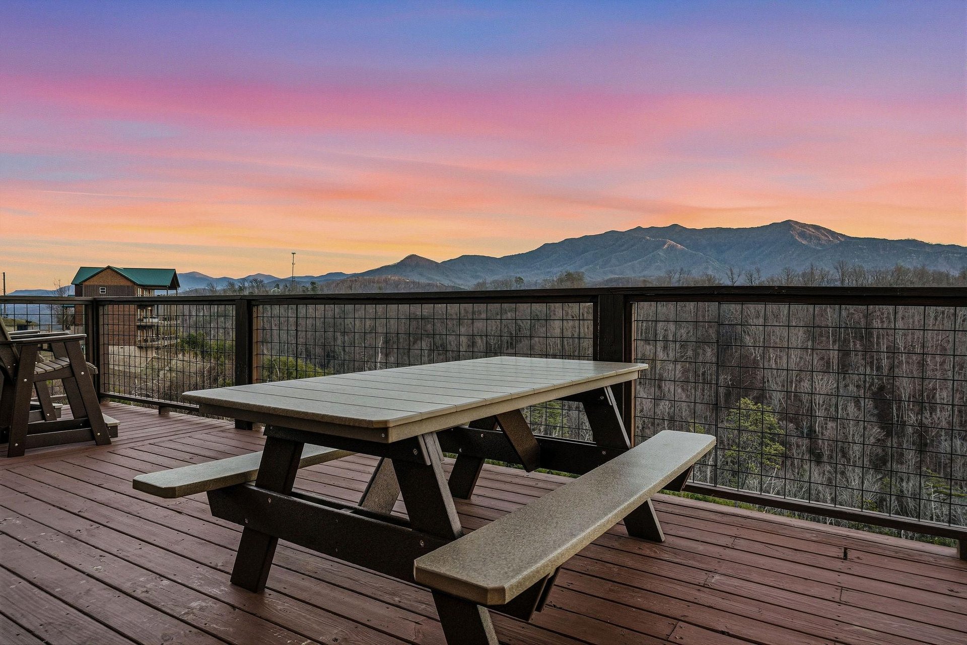 Stunning mountain sunrise paints the sky in brilliant colors above this elevated deck dining area, creating a breathtaking backdrop for the surrounding natural landscape.