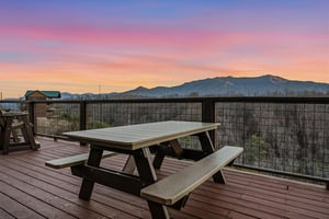 Stunning mountain sunrise paints the sky in brilliant colors above this elevated deck dining area, creating a breathtaking backdrop for the surrounding natural landscape.