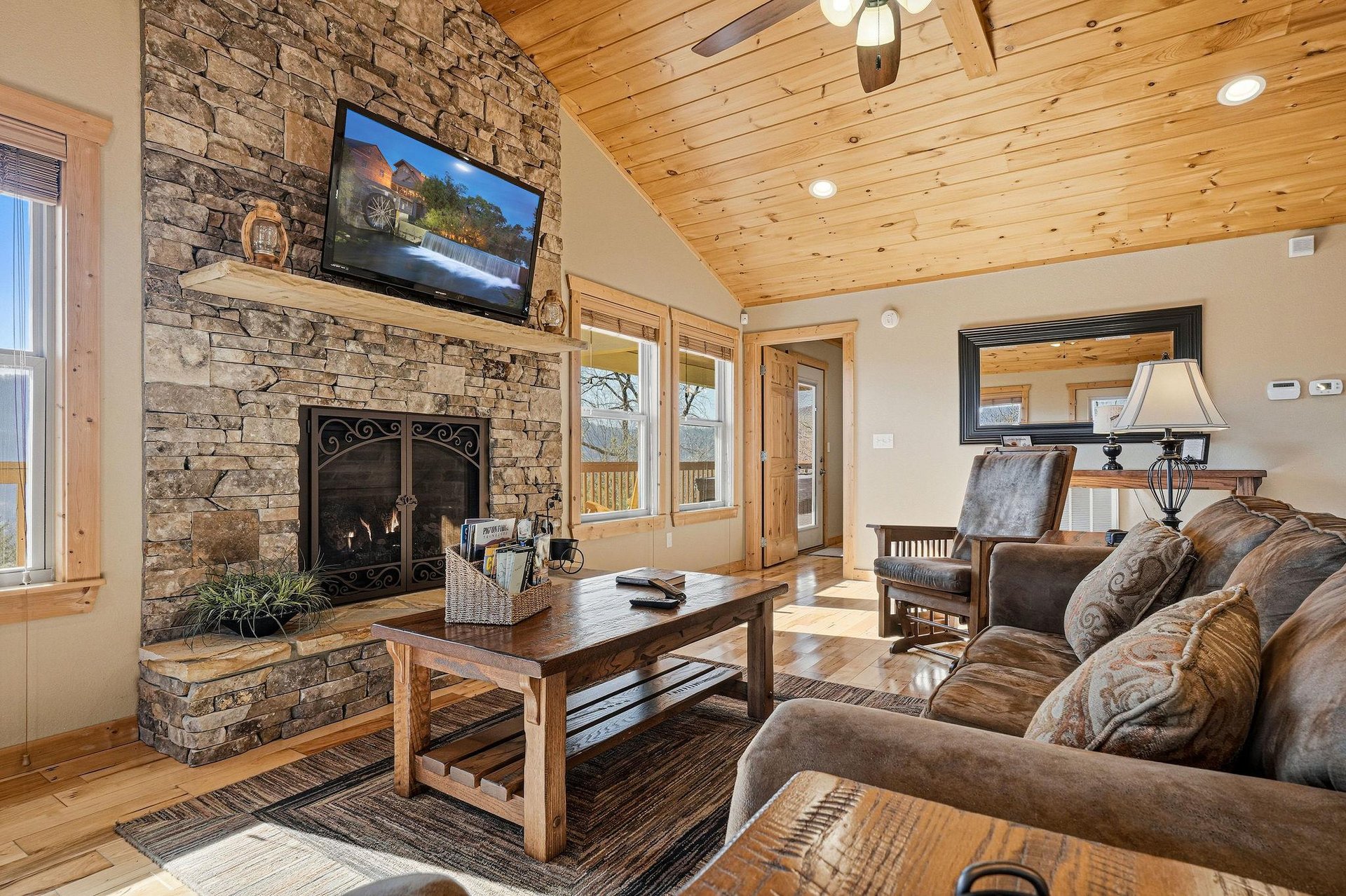 Unwind by your stone fireplace with warm wood beams overhead, cozy leather seating, and modern entertainment ready for relaxing mountain evenings.