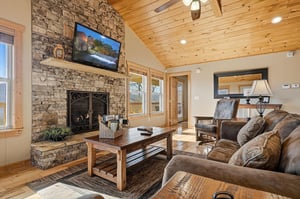 Unwind by your stone fireplace with warm wood beams overhead, cozy leather seating, and modern entertainment ready for relaxing mountain evenings.