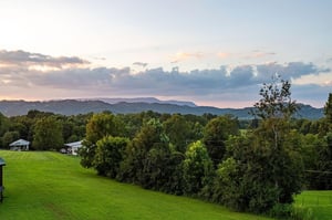 This property sits in a tranquil mountain setting with layered ridges and lush green surroundings, offering a peaceful rural escape as evening light softens the sky.