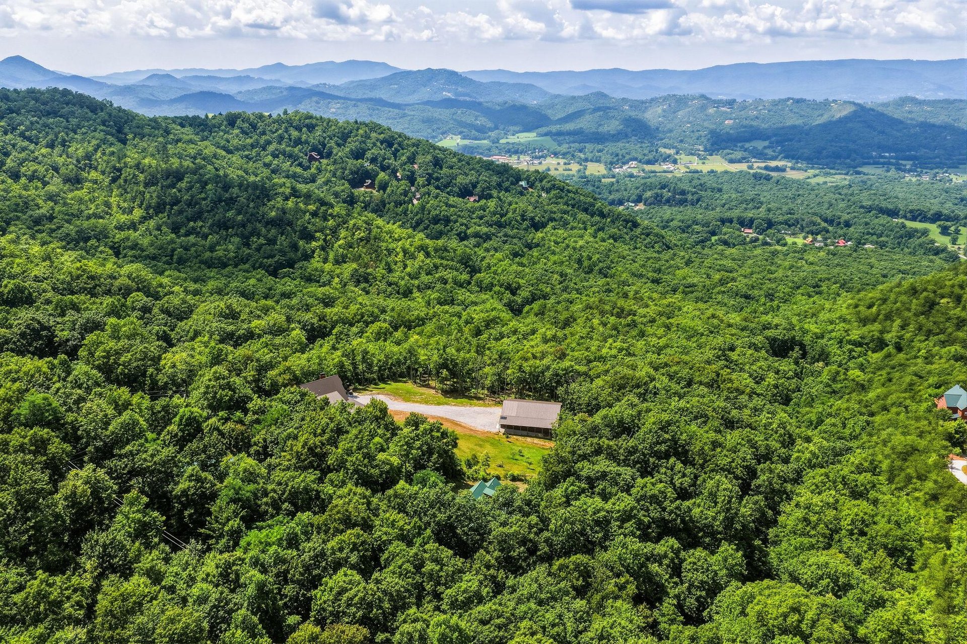 Aerial view of the property nestled in lush mountain forests, surrounded by rolling hills and peaceful valleys under expansive skies.