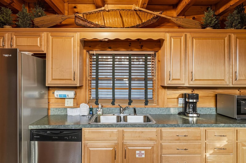 Your fully equipped kitchen features natural wood cabinetry and modern appliances, ready for you to prepare meals together in the warmth of this inviting log cabin space.
