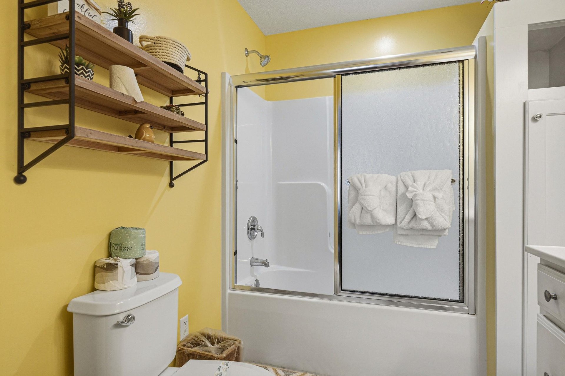 Refresh in your bright, cheerfully painted bathroom with a tubshower combo, fluffy towels, and thoughtful open shelving stocked with fresh linens and decorative touches for your comfort.