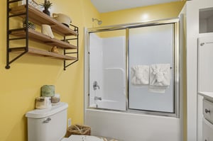 Refresh in your bright, cheerfully painted bathroom with a tubshower combo, fluffy towels, and thoughtful open shelving stocked with fresh linens and decorative touches for your comfort.