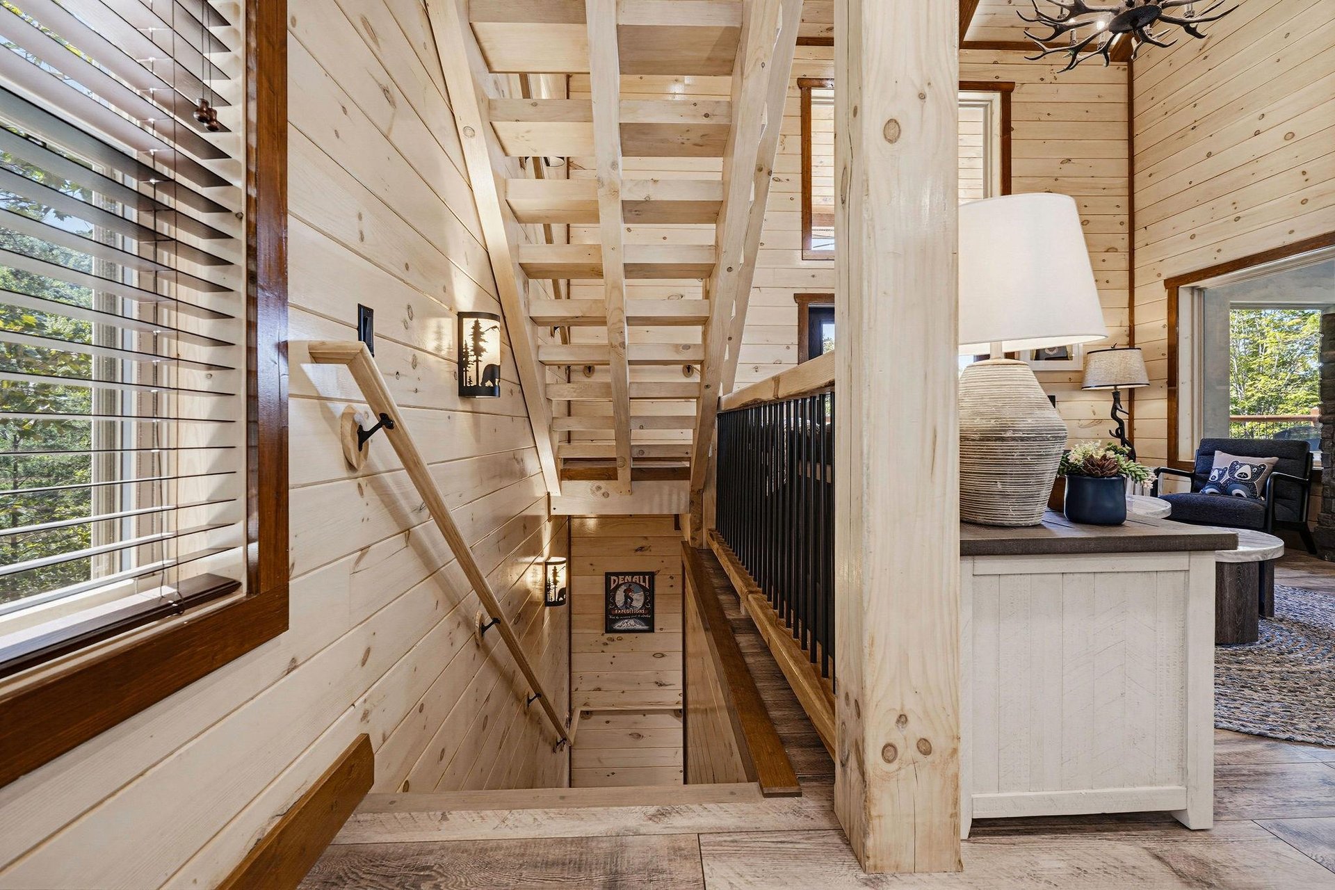 Natural light warms the woodpaneled staircase, where a rustic chandelier and glimpses of greenery through the windows invite you upward to your private retreat.