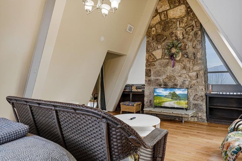 Relax in your charming attic living room featuring exposed stone walls, cozy wicker seating, and entertainment center.