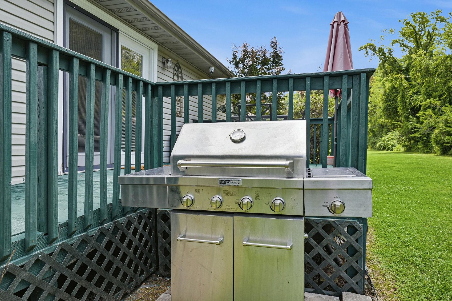 A stainless steel grill awaits on your private deck, ready for sunny afternoons cooking outdoors surrounded by lush green lawns and mature trees.