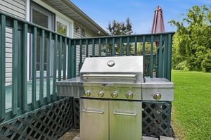 A stainless steel grill awaits on your private deck, ready for sunny afternoons cooking outdoors surrounded by lush green lawns and mature trees.