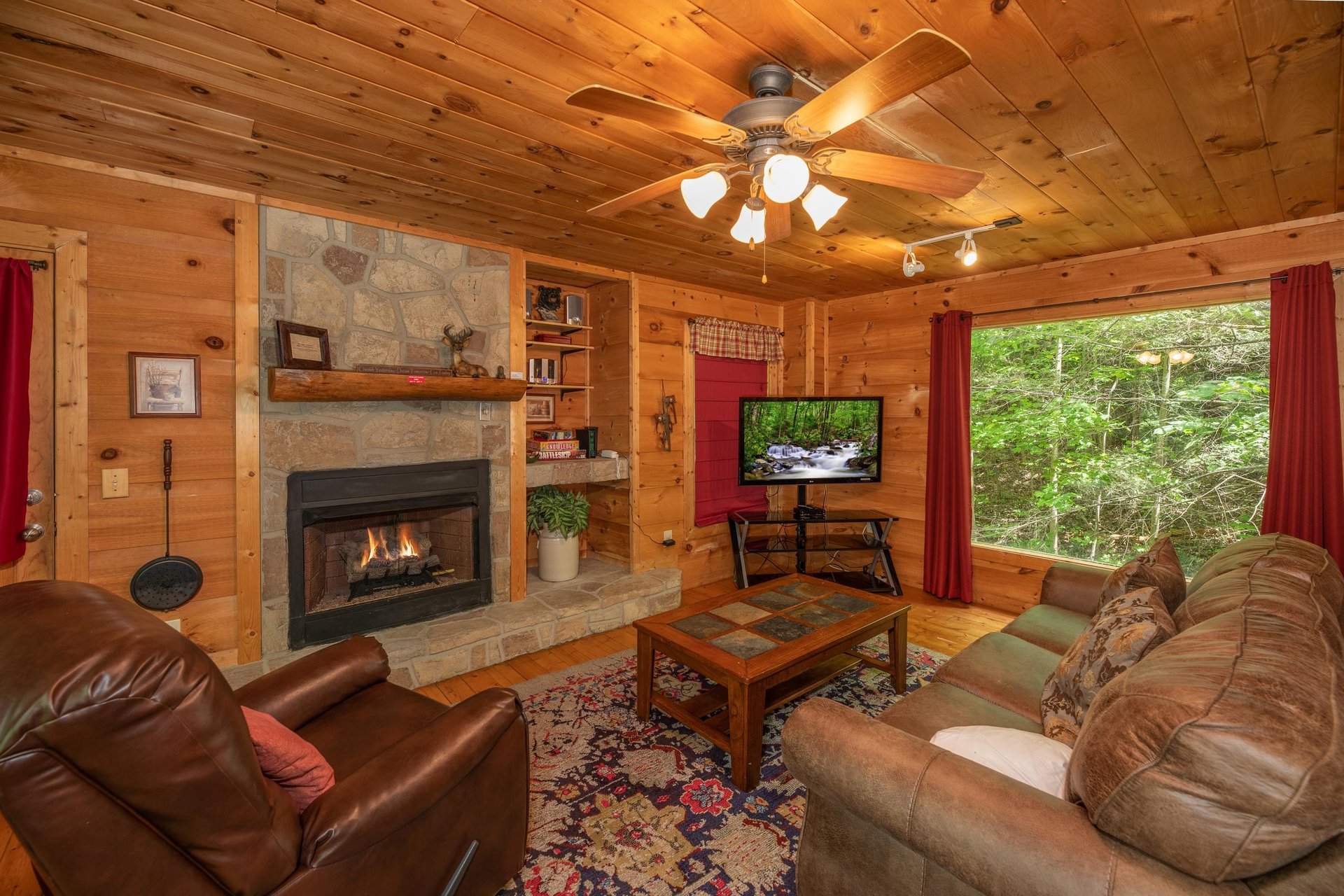 Fireplace, TV, and large picture window in the living room at Logans Smoky Den, a 2 bedroom cabin rental located in Pigeon Forge