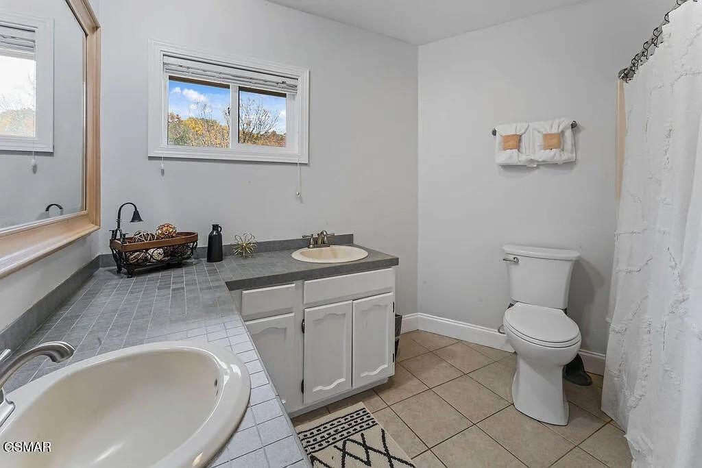 Unwind in your spacious bathroom featuring a deep soaking tub, marble shower, and peaceful autumn views through bright windows.