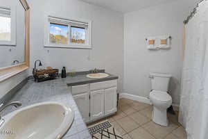Unwind in your spacious bathroom featuring a deep soaking tub, marble shower, and peaceful autumn views through bright windows.
