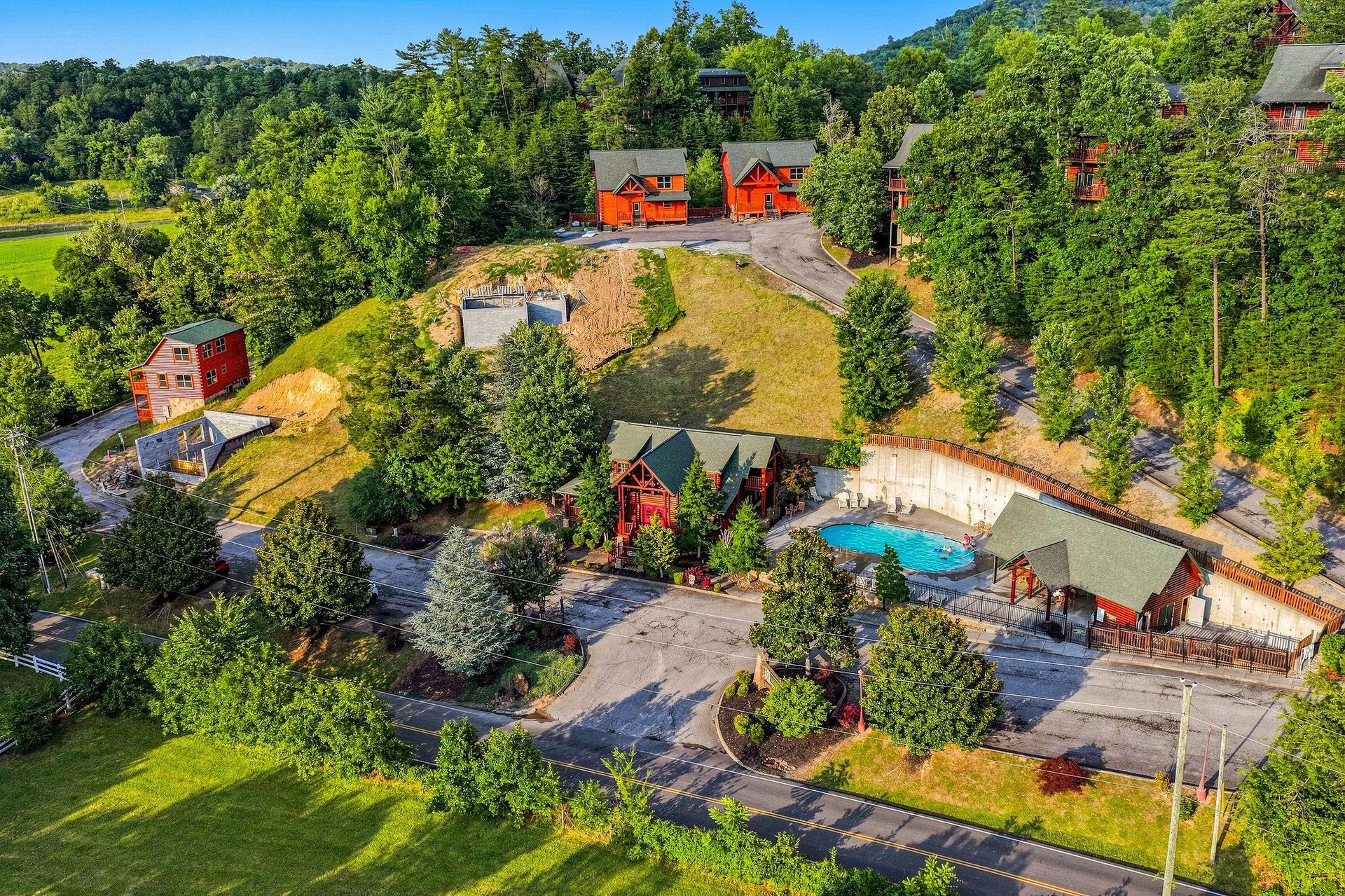 An aerial view showcases the vacation rental property nestled in lush mountain scenery, featuring multiple cabinstyle buildings, a refreshing pool area, and ample parking spaces surrounded by natural