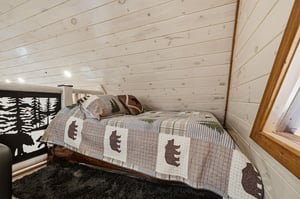 Cozy loft bedroom with rustic charm featuring bearthemed quilted bedding under beautiful exposed wood beams—your mountain retreat awaits.