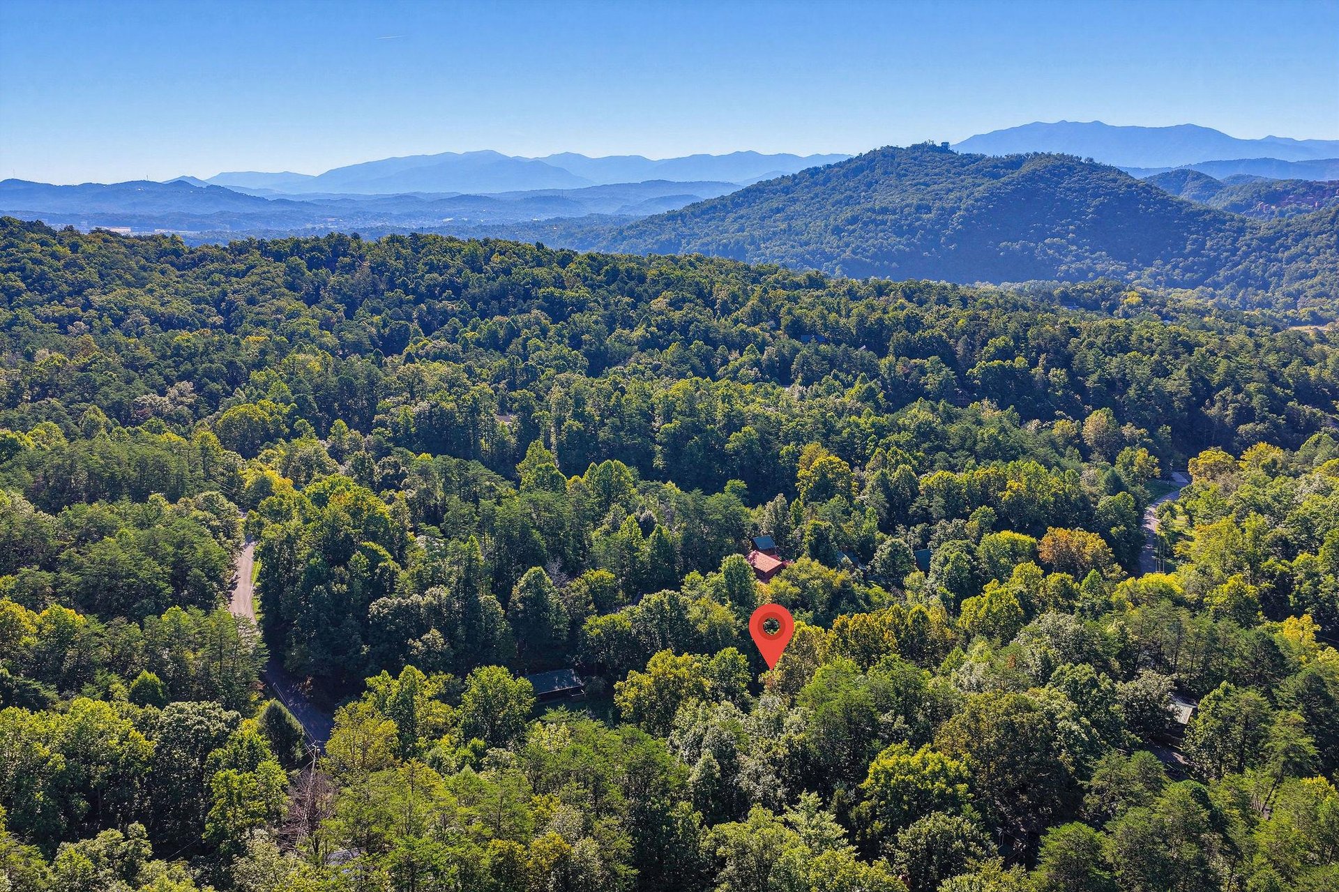 Aerial view of the property nestled in a forested mountain valley, surrounded by layered ridgelines and clear blue skies.