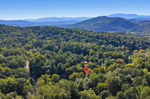Aerial view of the property nestled in a forested mountain valley, surrounded by layered ridgelines and clear blue skies.