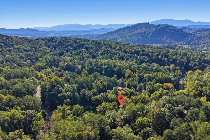 Aerial view of the property nestled in a forested mountain valley, surrounded by layered ridgelines and clear blue skies.